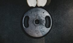 White running shoes beside a black weight plate, representing combined endurance and strength training