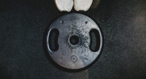 White running shoes beside a black weight plate, representing combined endurance and strength training