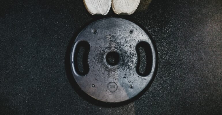 White running shoes beside a black weight plate, representing combined endurance and strength training