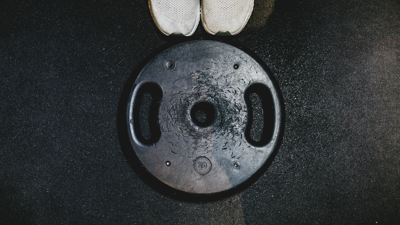 White running shoes beside a black weight plate, representing combined endurance and strength training