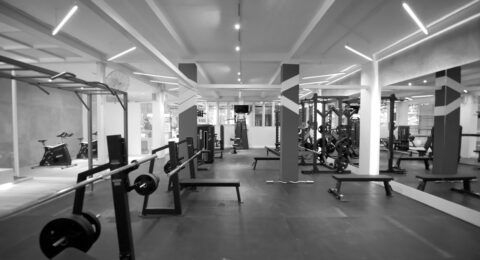 Barbell benches and weight plates in a gym, with resistance machines visible behind them.