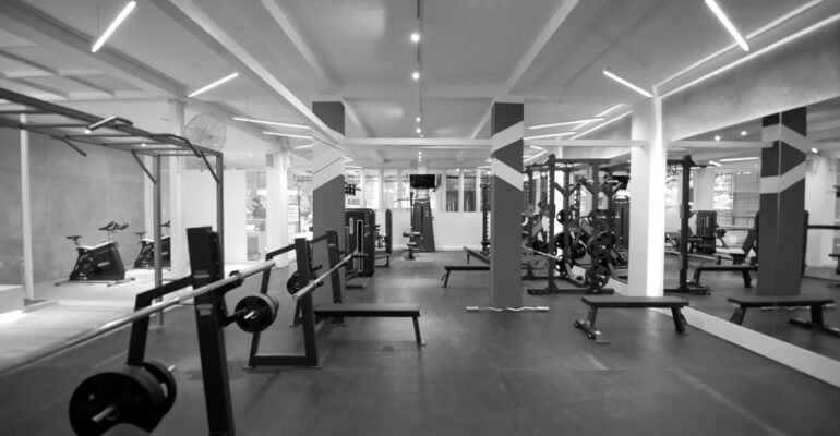 Barbell benches and weight plates in a gym, with resistance machines visible behind them.
