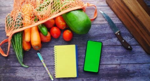 Fresh vegetables beside a notebook and phone used for planning a structured diet break