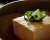 A block of tofu topped with sliced spring onions in a ceramic bowl