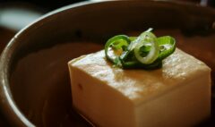 A block of tofu topped with sliced spring onions in a ceramic bowl