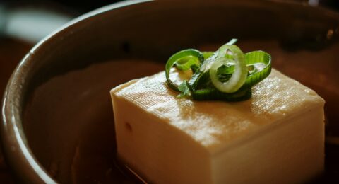A block of tofu topped with sliced spring onions in a ceramic bowl