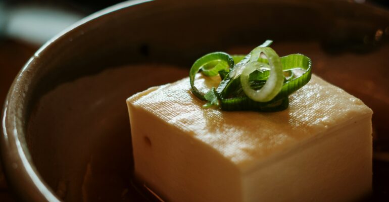 A block of tofu topped with sliced spring onions in a ceramic bowl