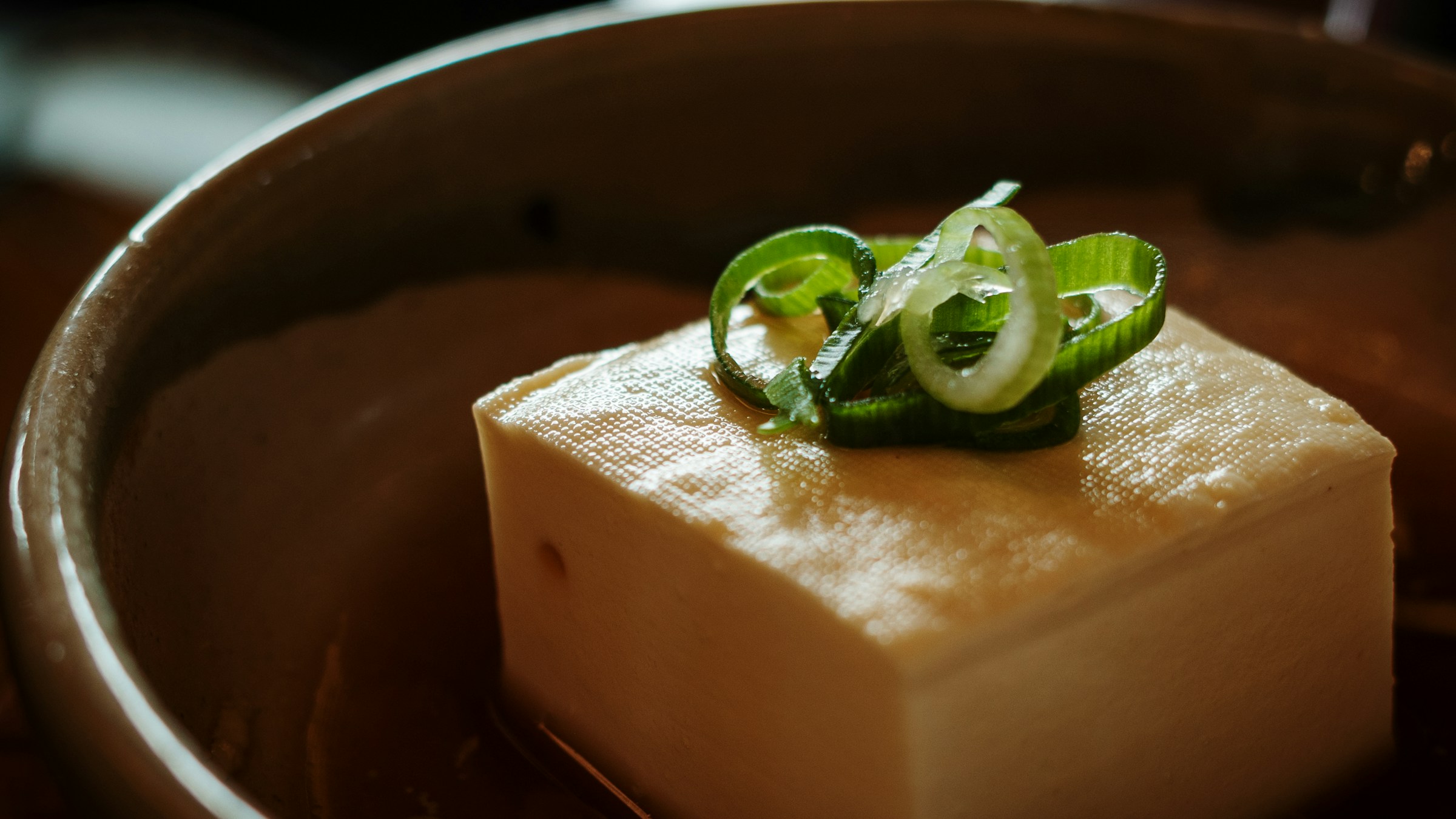 A block of tofu topped with sliced spring onions in a ceramic bowl