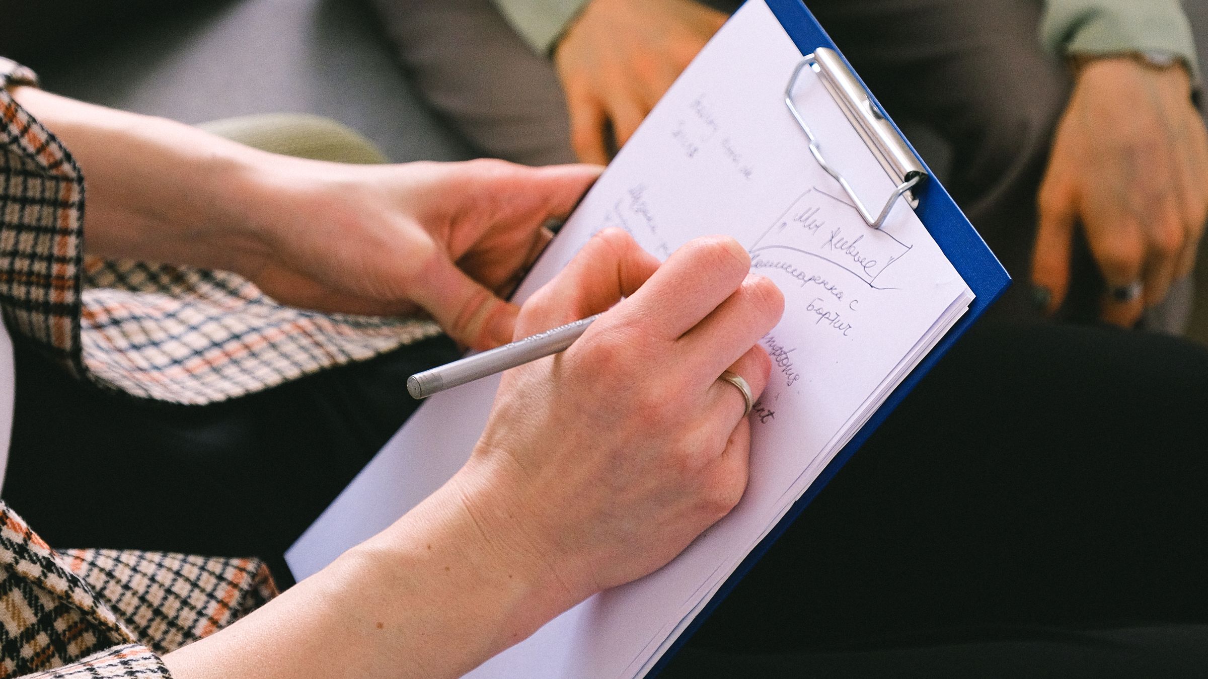 Close-up of a professional writing client notes on a clipboard during a conversation.