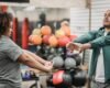 Adult client and fitness professional completing a standing warm-up in a gym