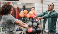 Adult client and fitness professional completing a standing warm-up in a gym