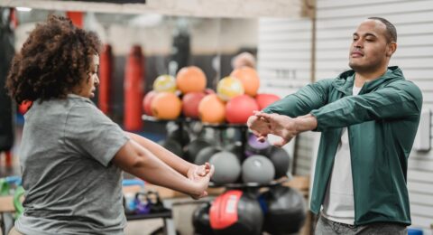 Adult client and fitness professional completing a standing warm-up in a gym
