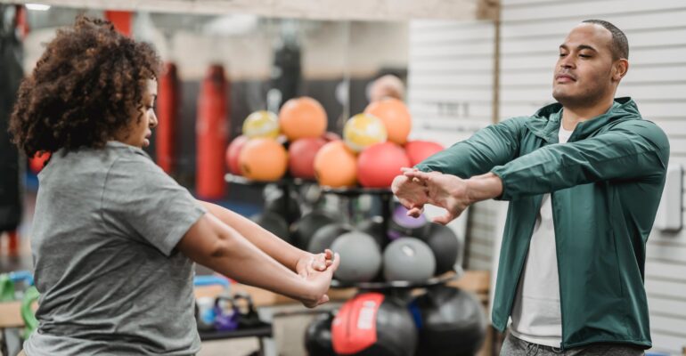 Adult client and fitness professional completing a standing warm-up in a gym