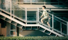An adult climbing an outdoor staircase beside a modern building during the day.