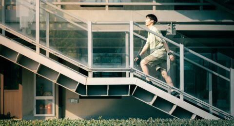 An adult climbing an outdoor staircase beside a modern building during the day.