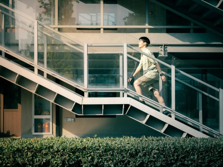 An adult climbing an outdoor staircase beside a modern building during the day.