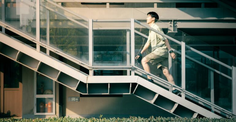 An adult climbing an outdoor staircase beside a modern building during the day.