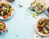 Colourful plates of beans, chickpeas and vegetables arranged on a light blue table.