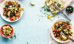 Colourful plates of beans, chickpeas and vegetables arranged on a light blue table.