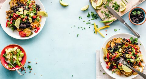 Colourful plates of beans, chickpeas and vegetables arranged on a light blue table.