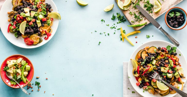 Colourful plates of beans, chickpeas and vegetables arranged on a light blue table.