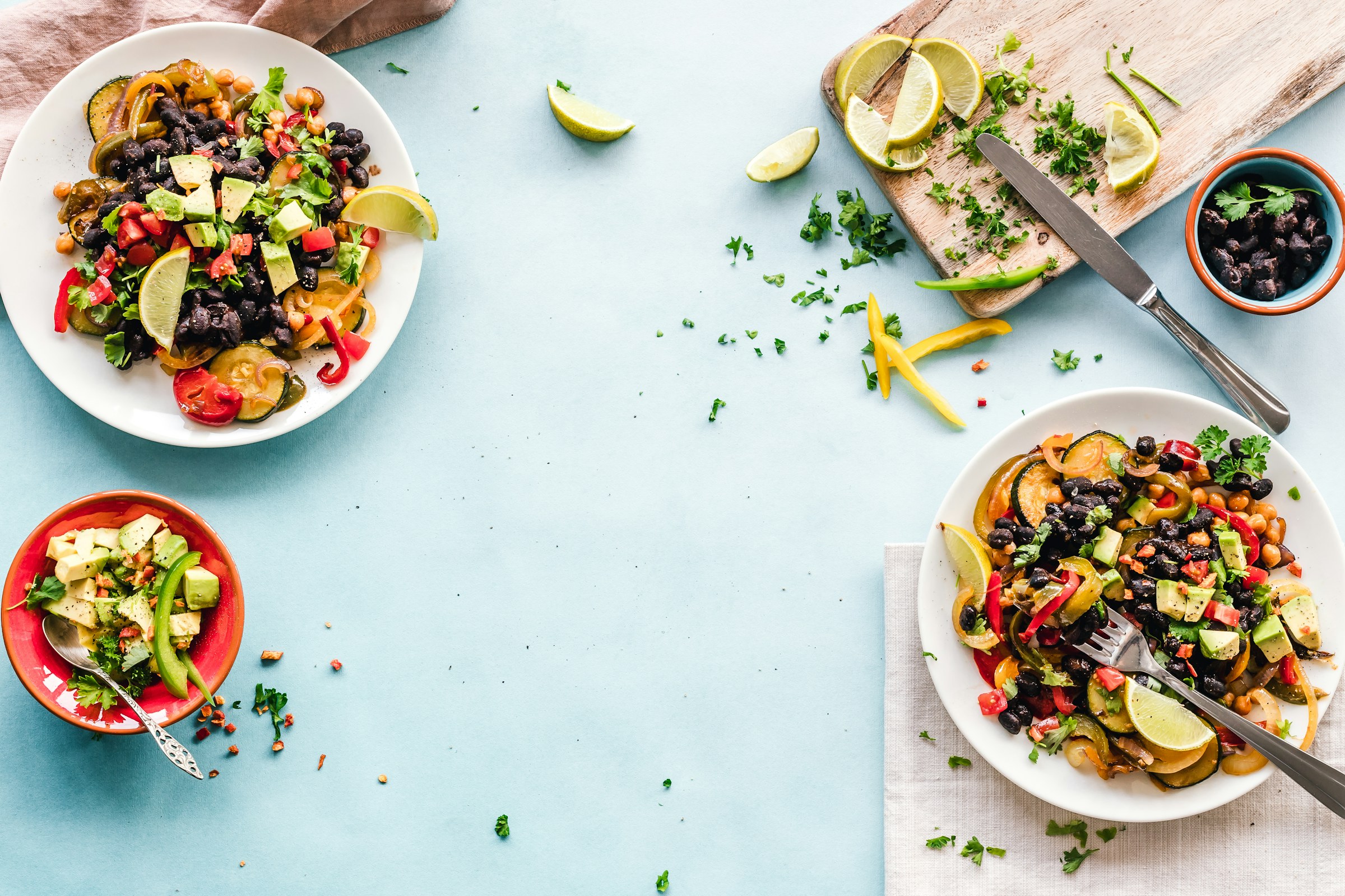Colourful plates of beans, chickpeas and vegetables arranged on a light blue table.