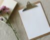 A blank consultation form on a clipboard beside a notebook and flowers, representing informed consent before massage.