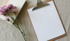 A blank consultation form on a clipboard beside a notebook and flowers, representing informed consent before massage.