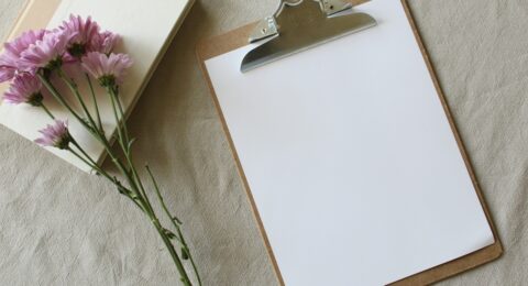 A blank consultation form on a clipboard beside a notebook and flowers, representing informed consent before massage.