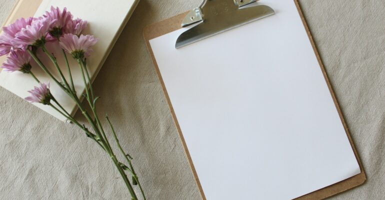 A blank consultation form on a clipboard beside a notebook and flowers, representing informed consent before massage.