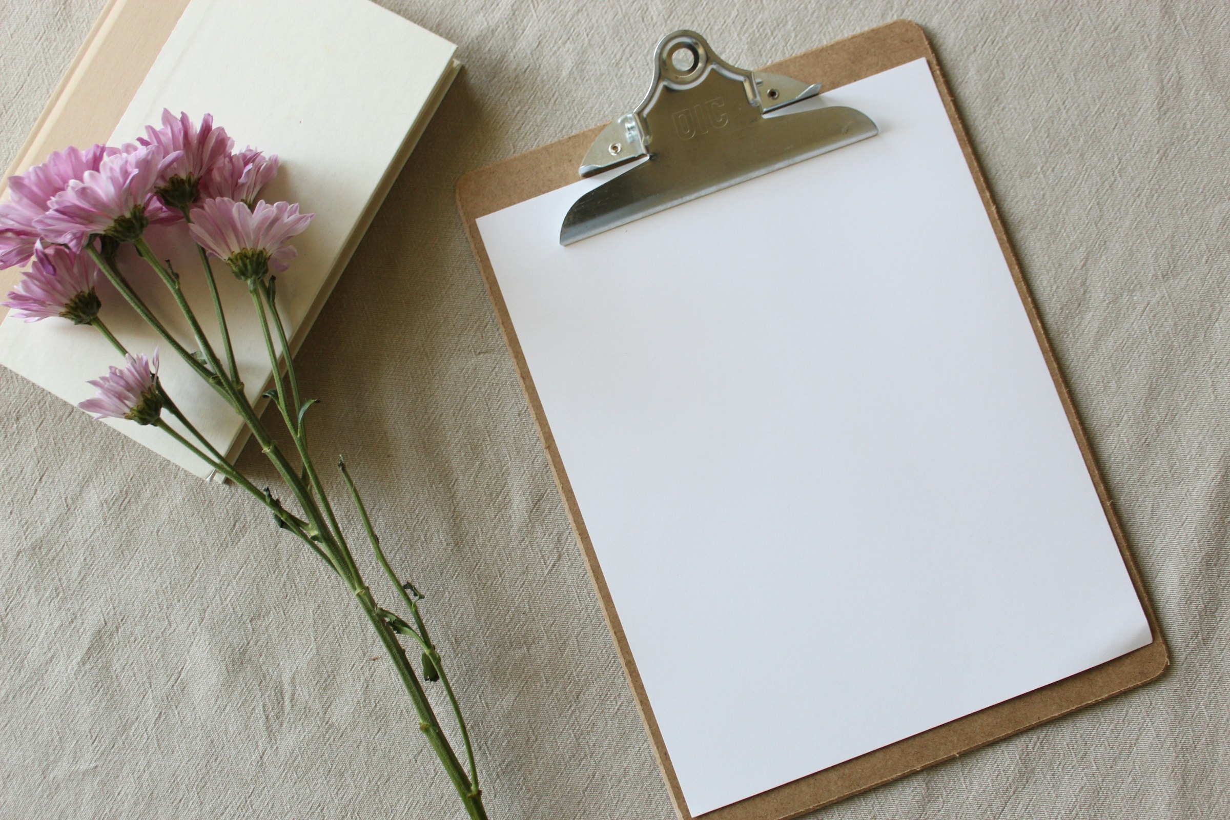 A blank consultation form on a clipboard beside a notebook and flowers, representing informed consent before massage.