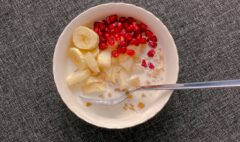 A bowl of oats with milk, banana, apple and pomegranate, viewed from above.