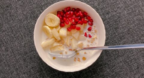 A bowl of oats with milk, banana, apple and pomegranate, viewed from above.