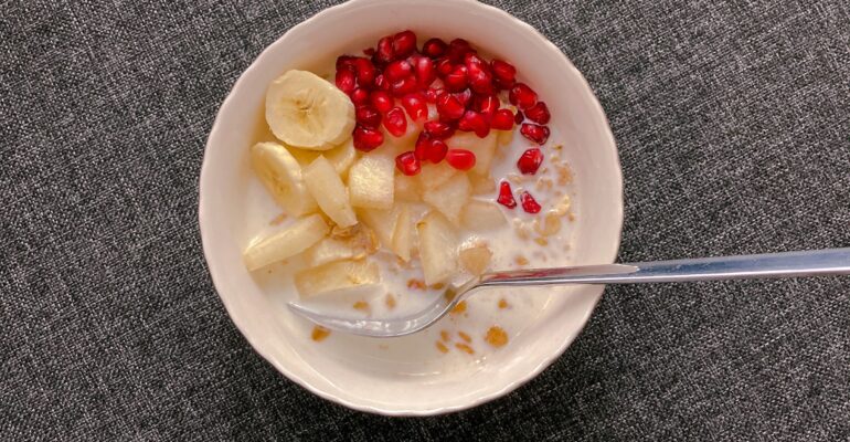 A bowl of oats with milk, banana, apple and pomegranate, viewed from above.
