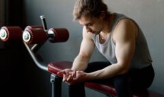 An adult exerciser sitting on a gym bench during a rest interval.