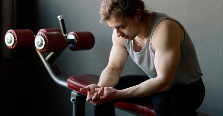 An adult exerciser sitting on a gym bench during a rest interval.