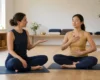 A yoga teacher using a gentle hand cue to pace slow breathing with an adult student in a bright studio