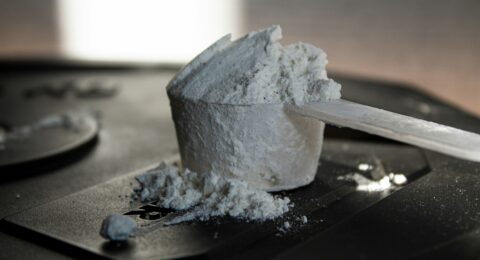 An unlabelled scoop of supplement powder on a dark surface, representing uncertainty about supplement contents.