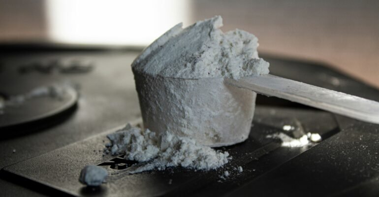 An unlabelled scoop of supplement powder on a dark surface, representing uncertainty about supplement contents.