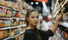 An adult shopper considering products in a supermarket aisle filled with packaged foods.