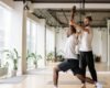 Yoga teacher guiding an adult student through a controlled standing pose in a bright studio