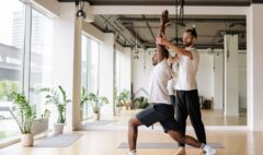 Yoga teacher guiding an adult student through a controlled standing pose in a bright studio