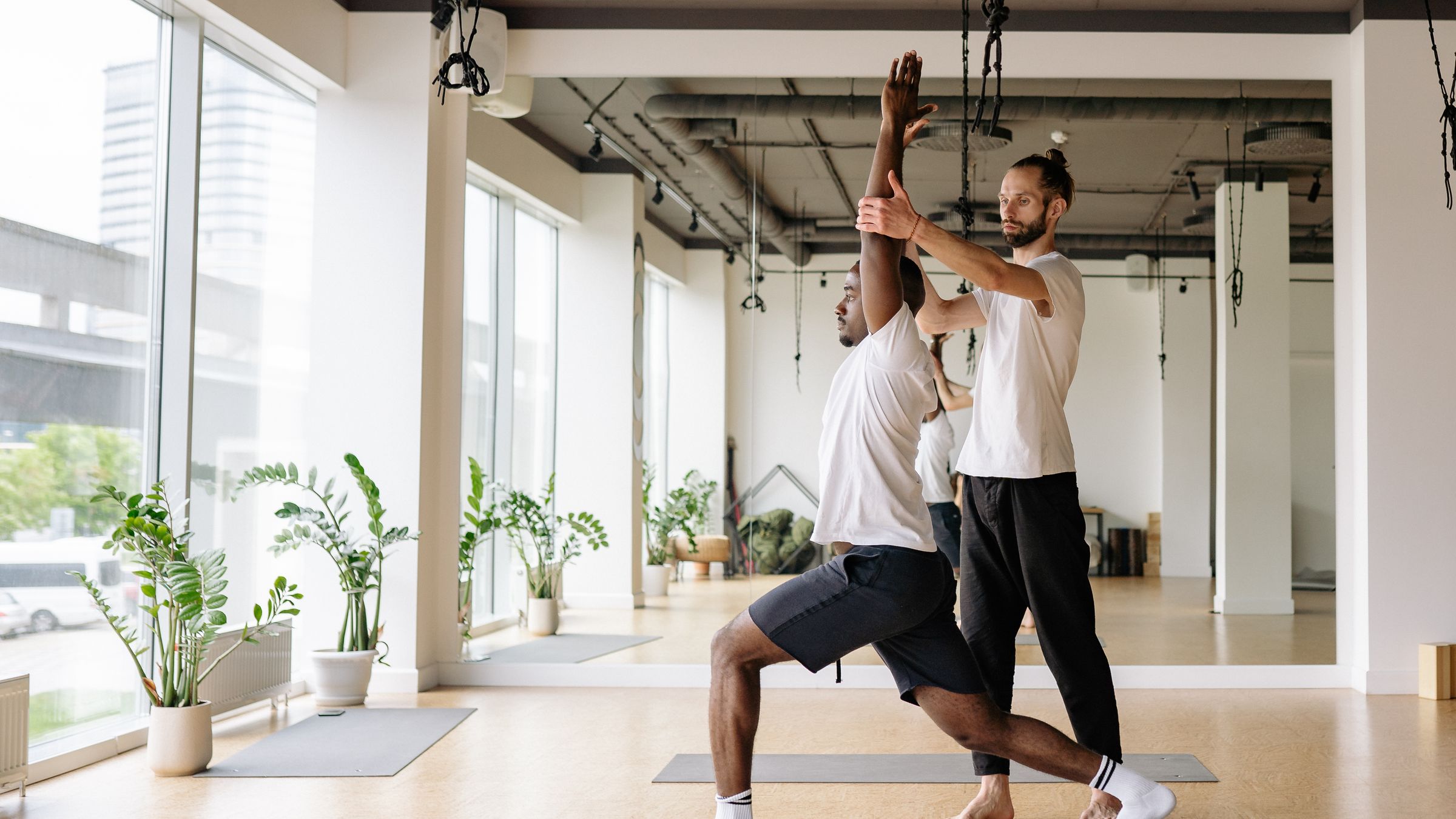Yoga teacher guiding an adult student through a controlled standing pose in a bright studio