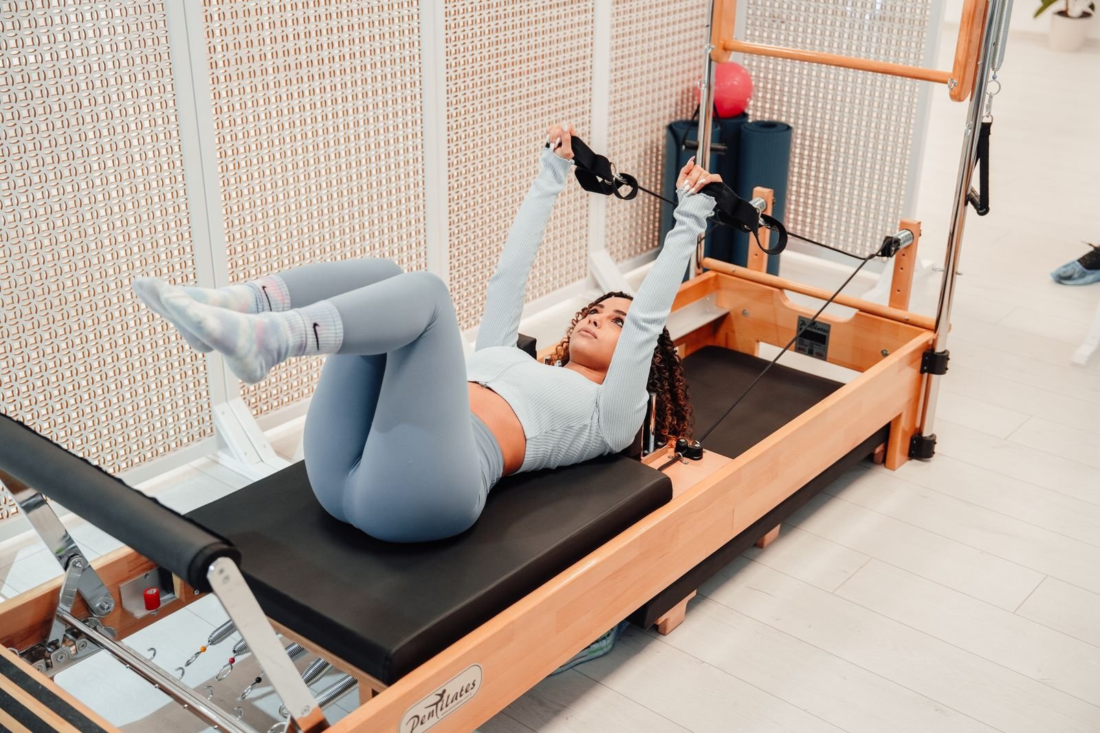 Woman exercising with straps on a wooden Pilates Reformer