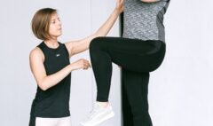 Older adult practising a supported standing balance exercise with an instructor nearby