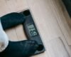 A person in socks standing on a digital bathroom scale on a wooden floor.