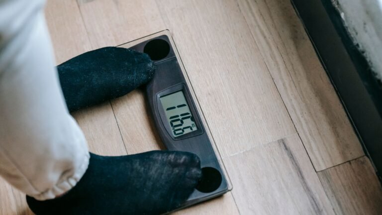 A person in socks standing on a digital bathroom scale on a wooden floor.