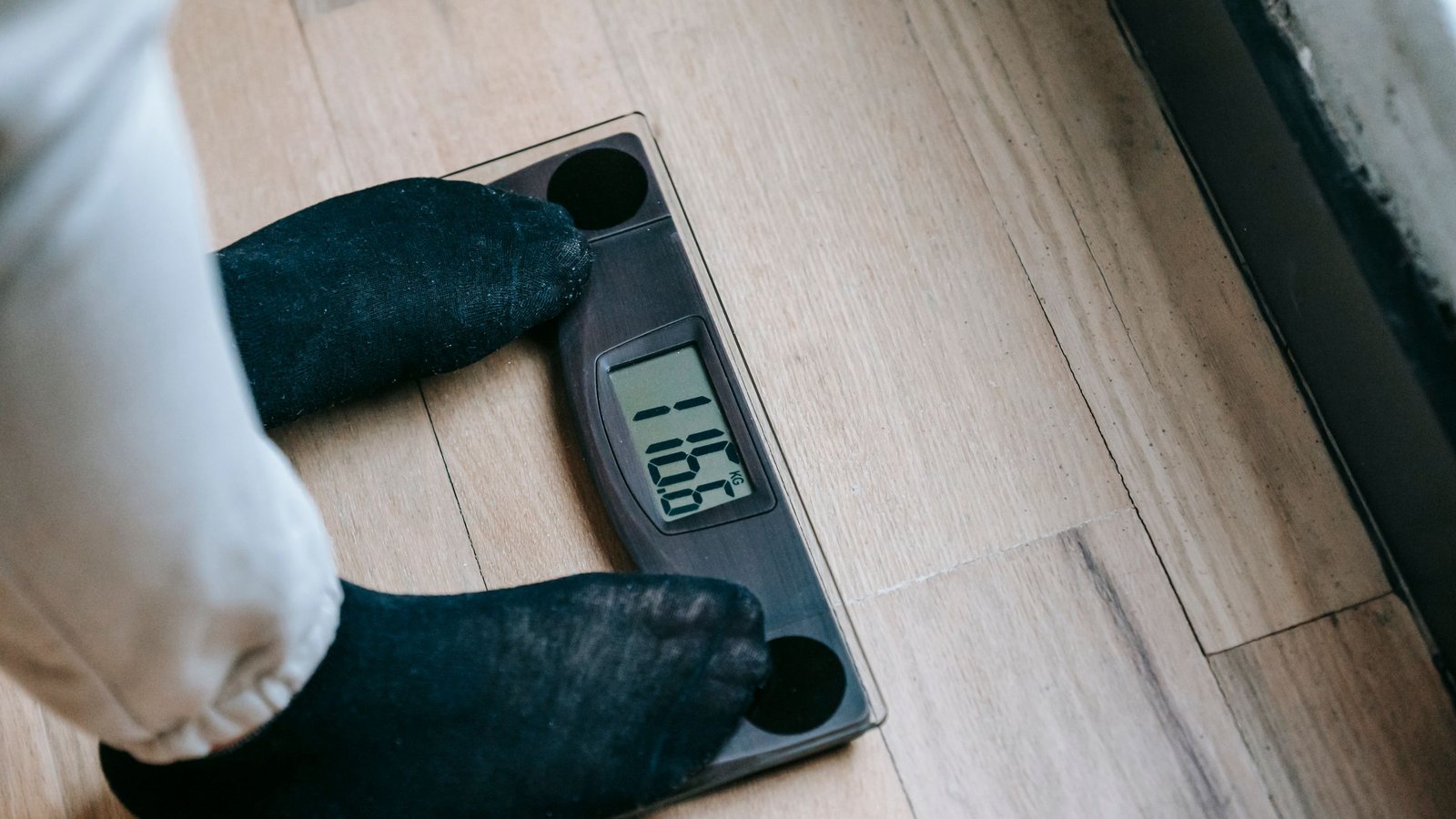 A person in socks standing on a digital bathroom scale on a wooden floor.
