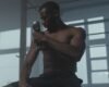 Man using a handheld massage gun on his upper arm in a gym