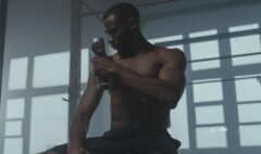 Man using a handheld massage gun on his upper arm in a gym